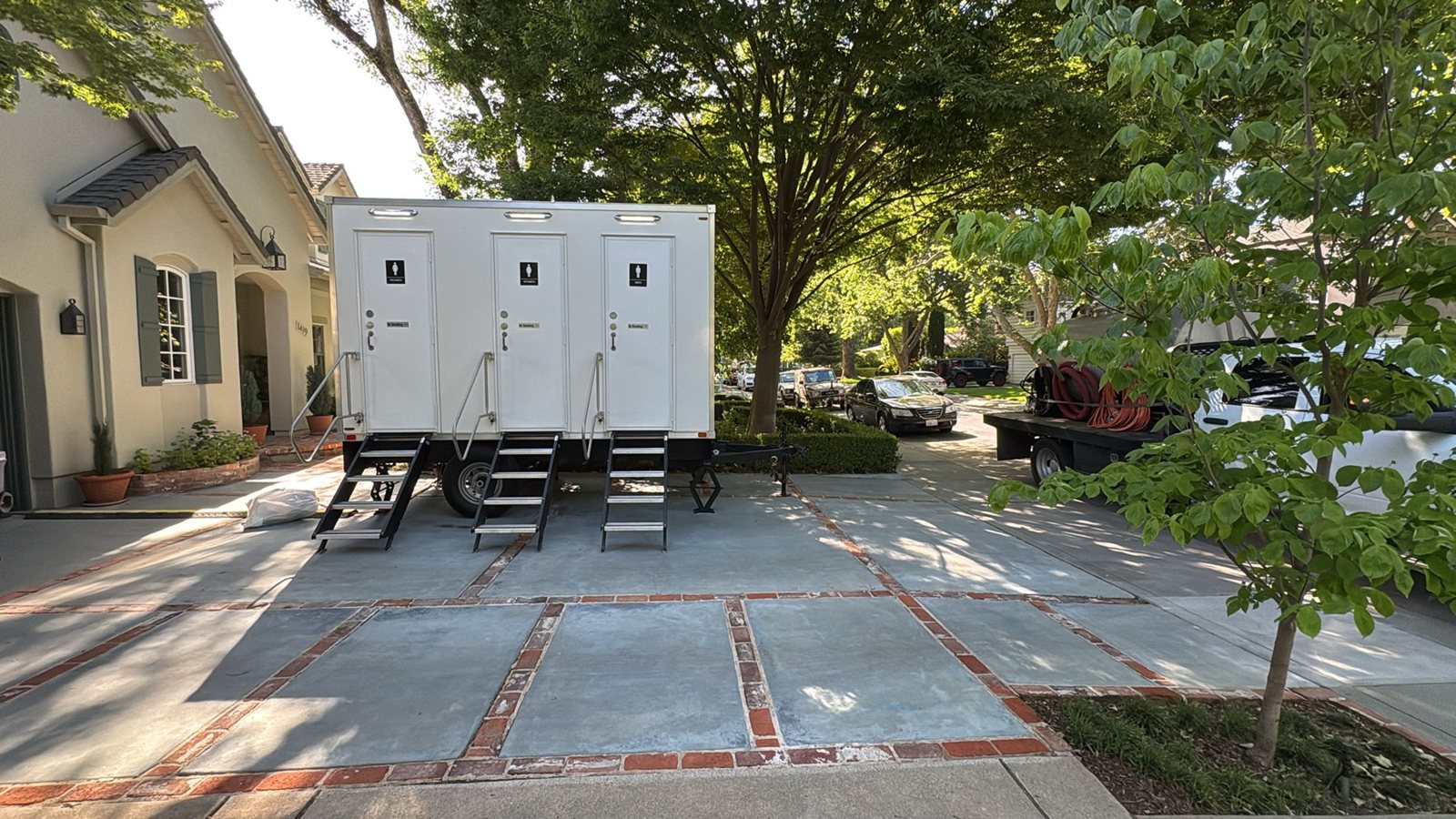 A three station Lavatory restroom trailer set on a home driveway under shade trees, with steps at each door