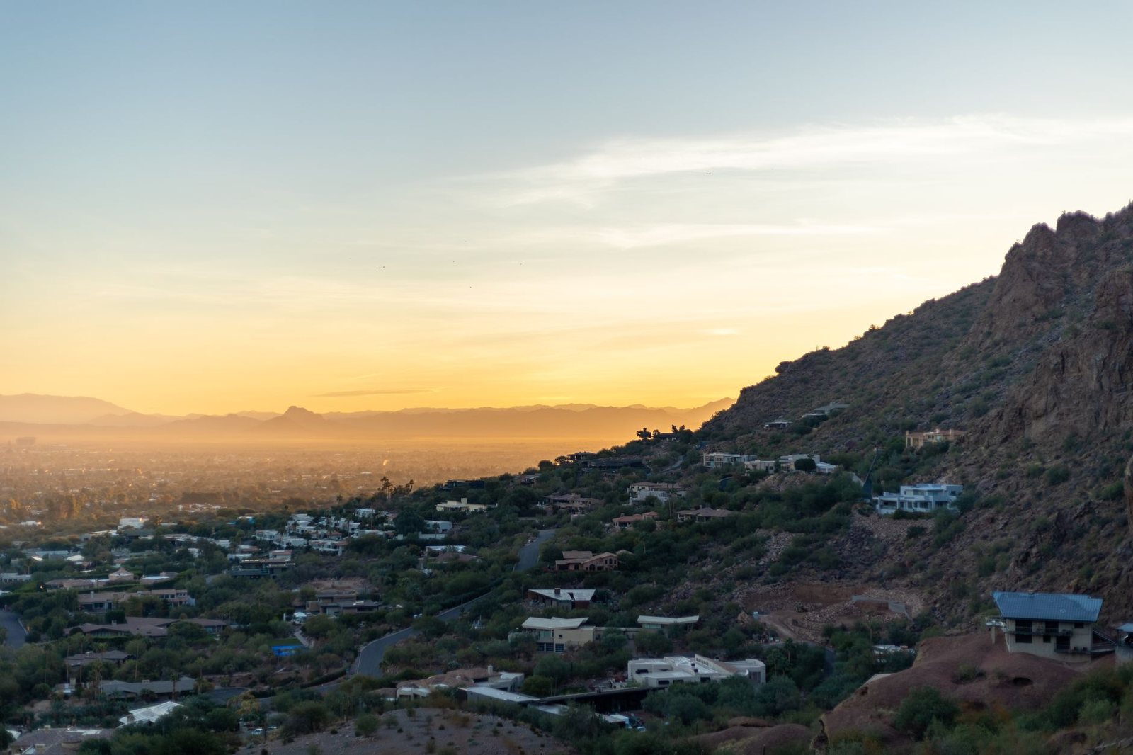 Hillside homes on a rocky desert mountain above the Phoenix valley at sunset