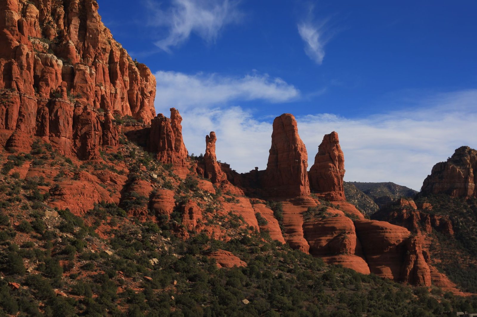 Red rock spires and cliffs above juniper-covered slopes in Sedona under a blue sky