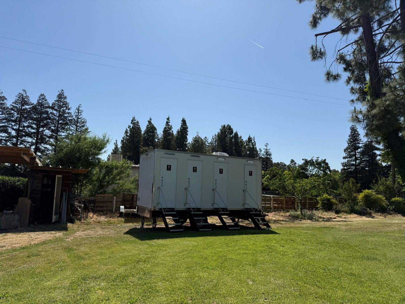 A Lavatory 4-Station luxury restroom trailer on a green backyard lawn with pine trees behind it in Clovis