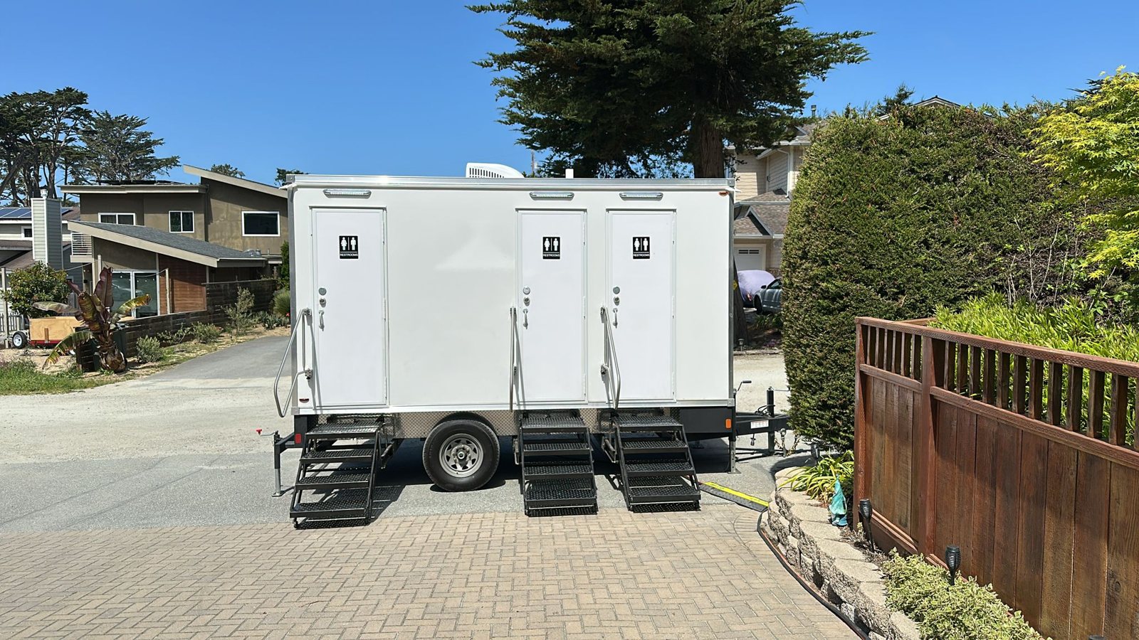 A Lavatory 3-Station restroom trailer parked on a paver driveway on a residential street