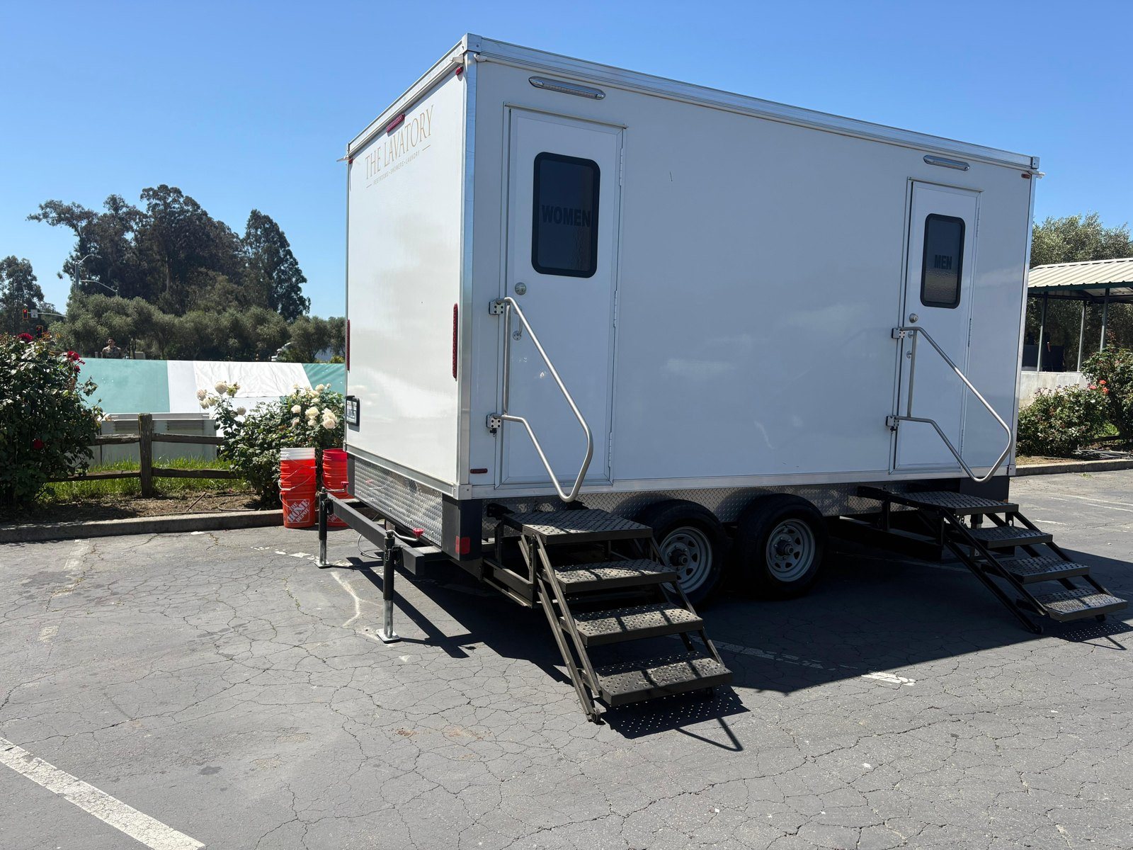 A Lavatory 5-Station restroom trailer parked in a paved event lot, with white event tents and trees behind it