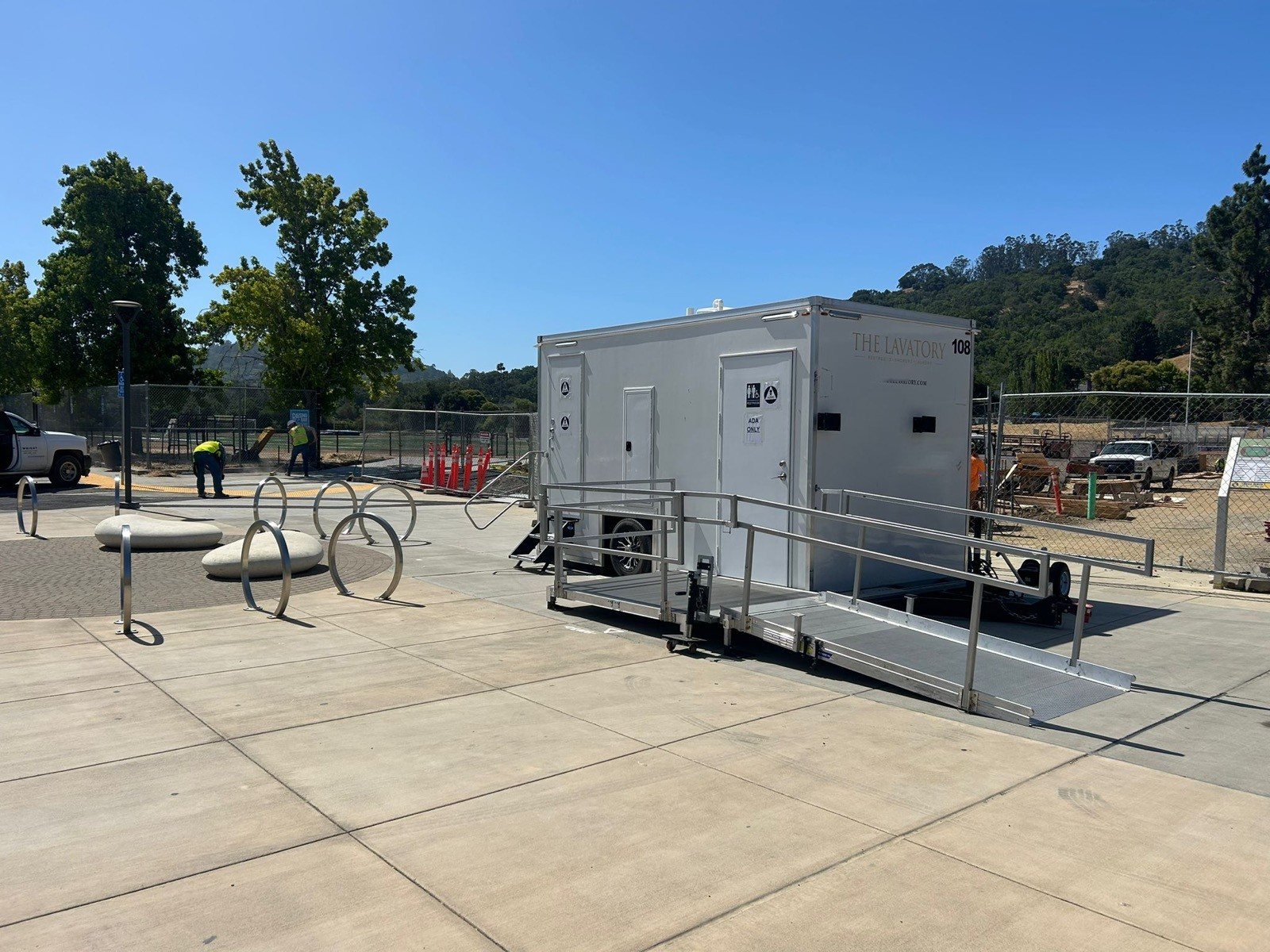 A Lavatory ADA restroom trailer with a ramp on a concrete plaza beside bike racks