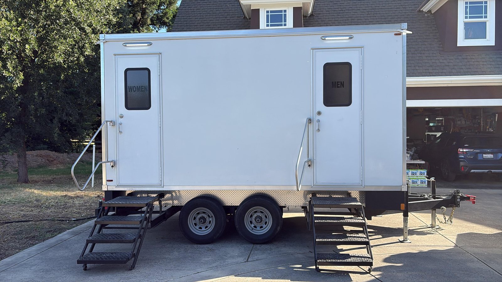 A Lavatory restroom trailer parked on a home driveway in front of a garage