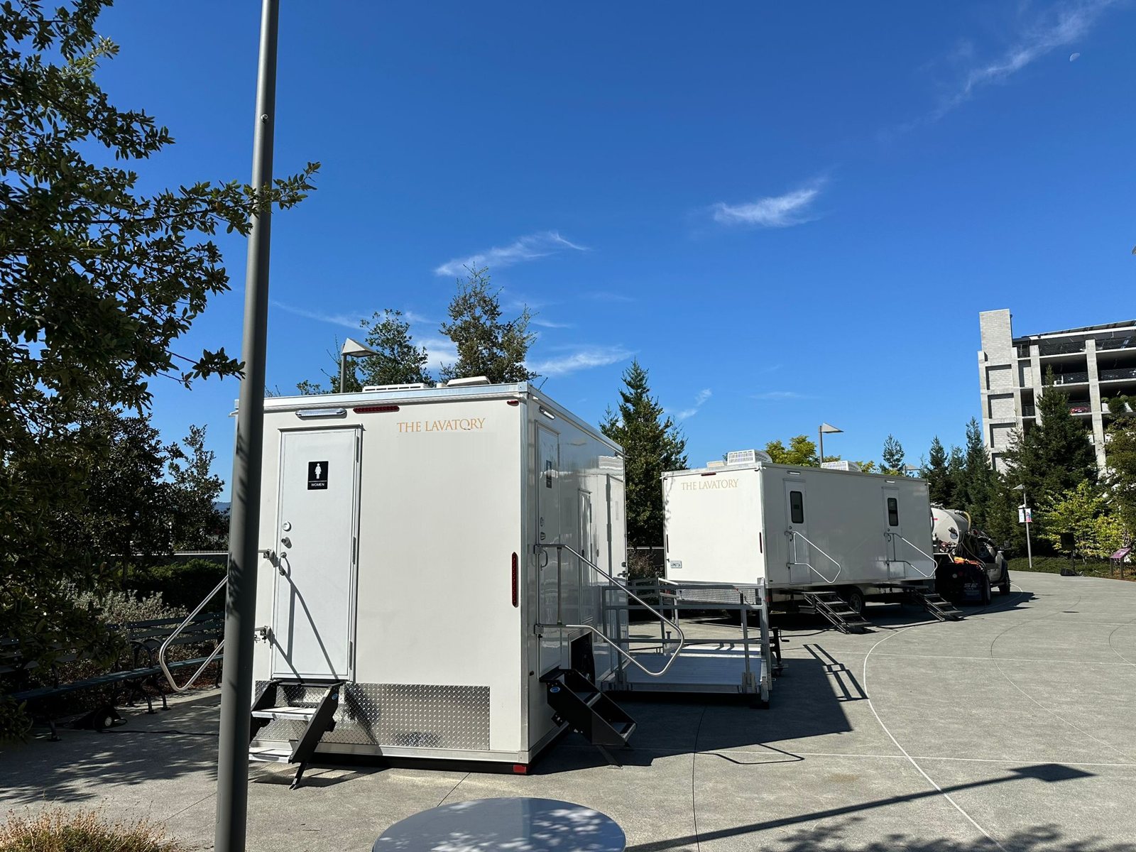 A Lavatory 2-Station restroom trailer and an ADA restroom trailer with its ramp set up on a paved plaza at an office campus in Palo Alto