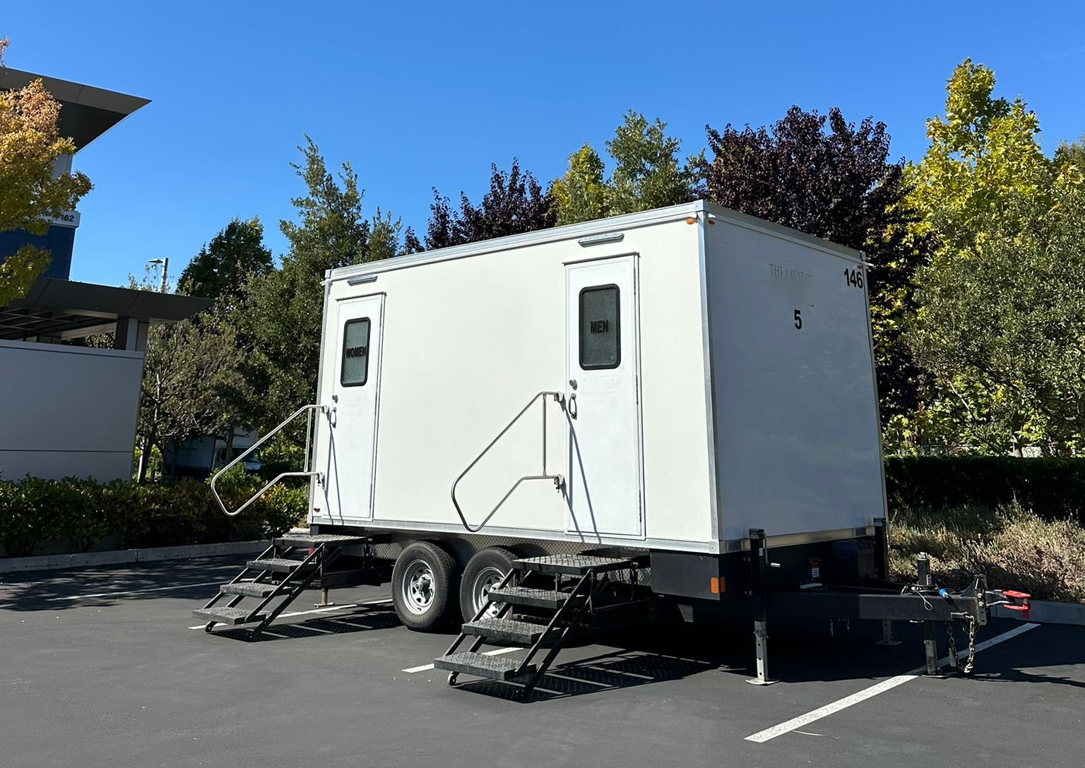 A Lavatory 2-Station restroom trailer with women's and men's doors in an office campus parking lot in Palo Alto