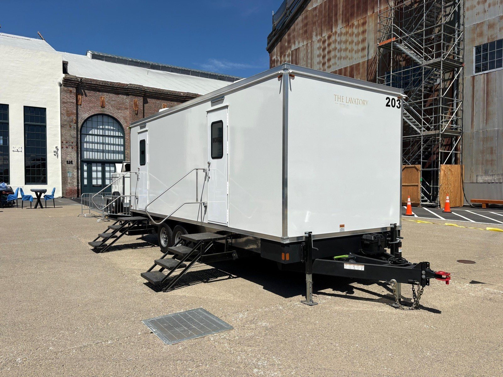 A Lavatory restroom trailer parked beside a historic brick building with scaffolding on its facade