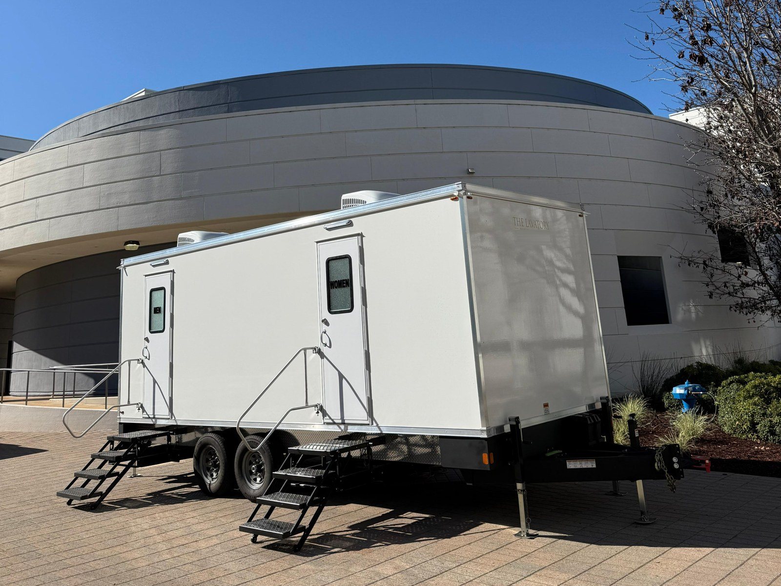A Lavatory 9-Station restroom trailer on a brick plaza outside a curved corporate building in Redwood City
