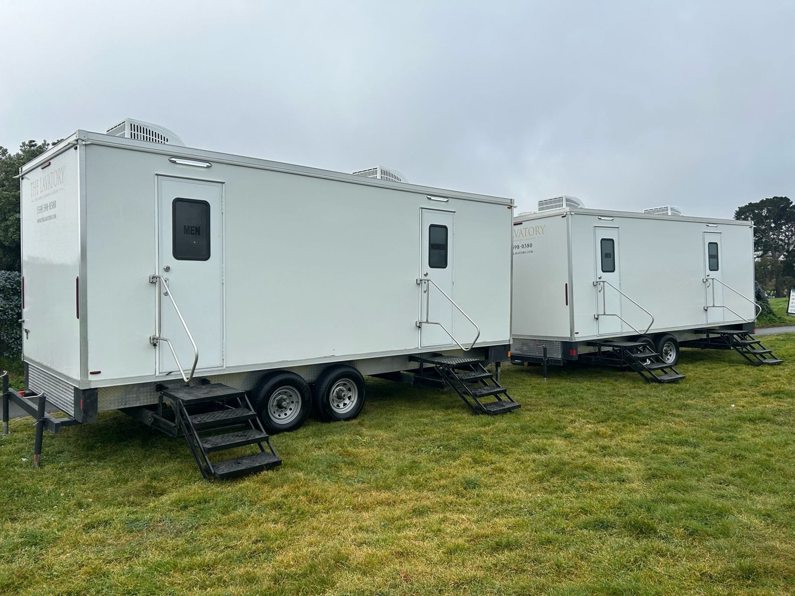 Two Lavatory restroom trailers with men and women doors set side by side on a grass field