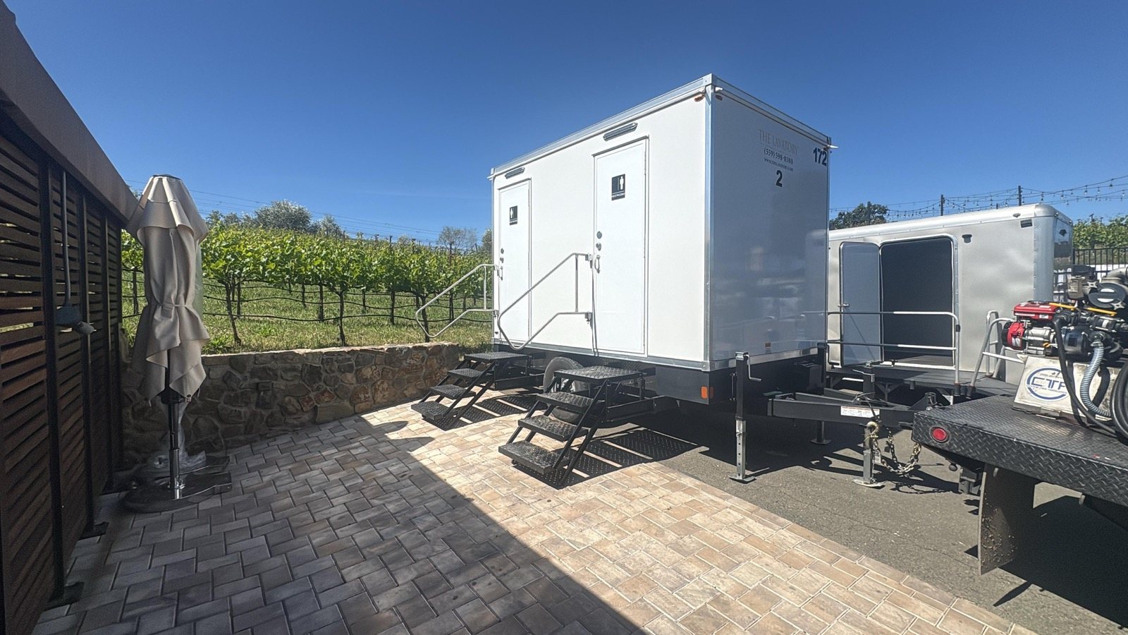 A Lavatory 2-Station restroom trailer on a brick terrace at a winery, with grapevines on the hillside behind it