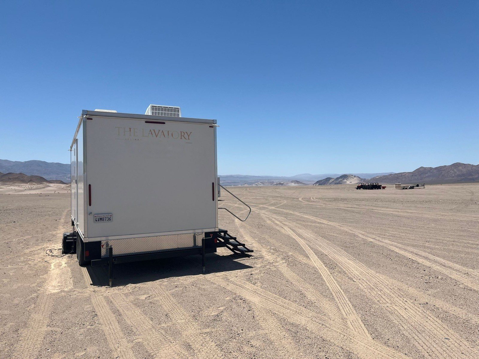A Lavatory restroom trailer parked on open graded dirt at a high desert job site, with low mountains in the distance