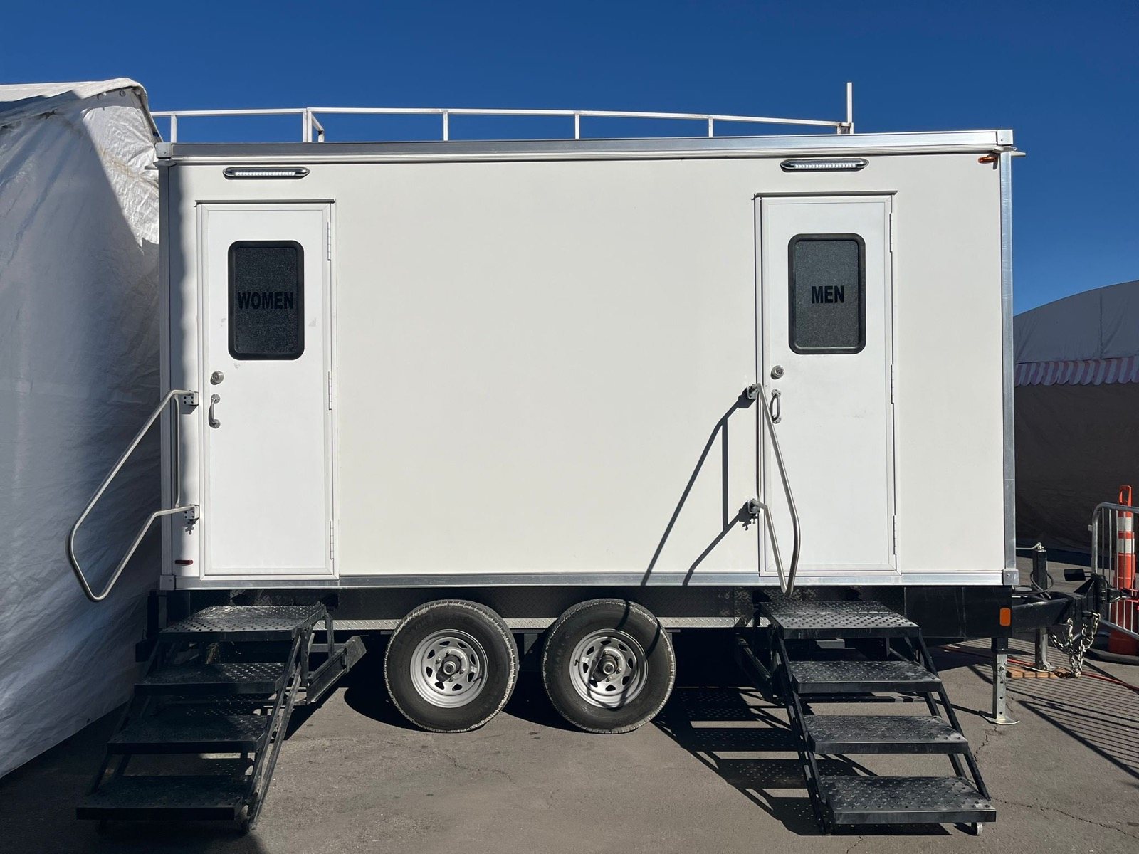 A Lavatory 2-Station restroom trailer with separate women's and men's doors set up beside a white event tent