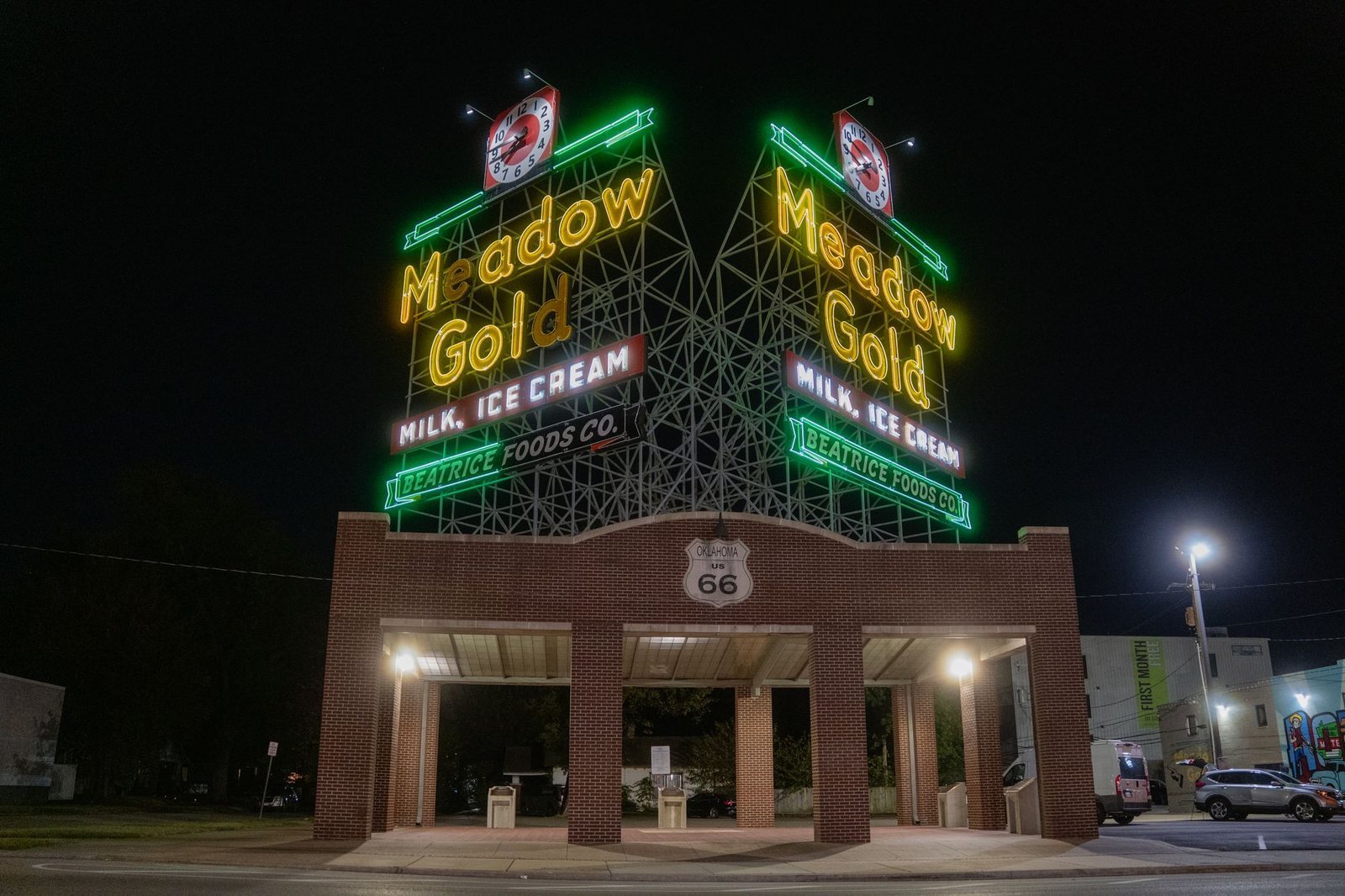 The Meadow Gold neon sign lit at night above its brick pavilion on Route 66 in Tulsa
