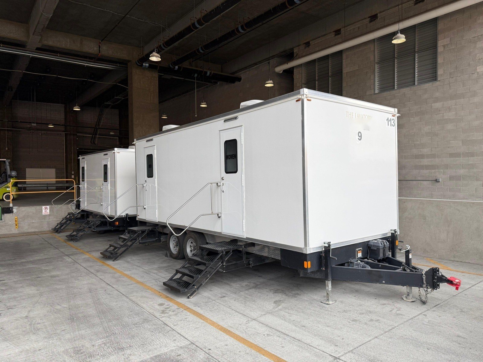 Two Lavatory 9-Station restroom trailers parked side by side at a covered loading dock