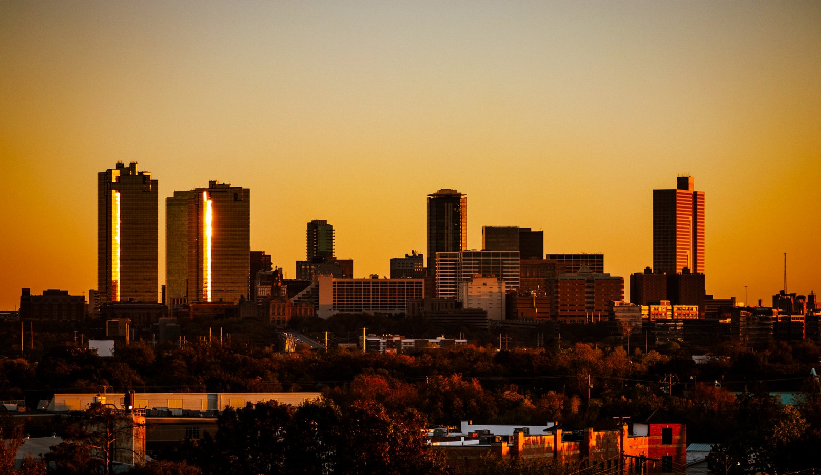 The downtown Fort Worth skyline at sunset above a line of trees