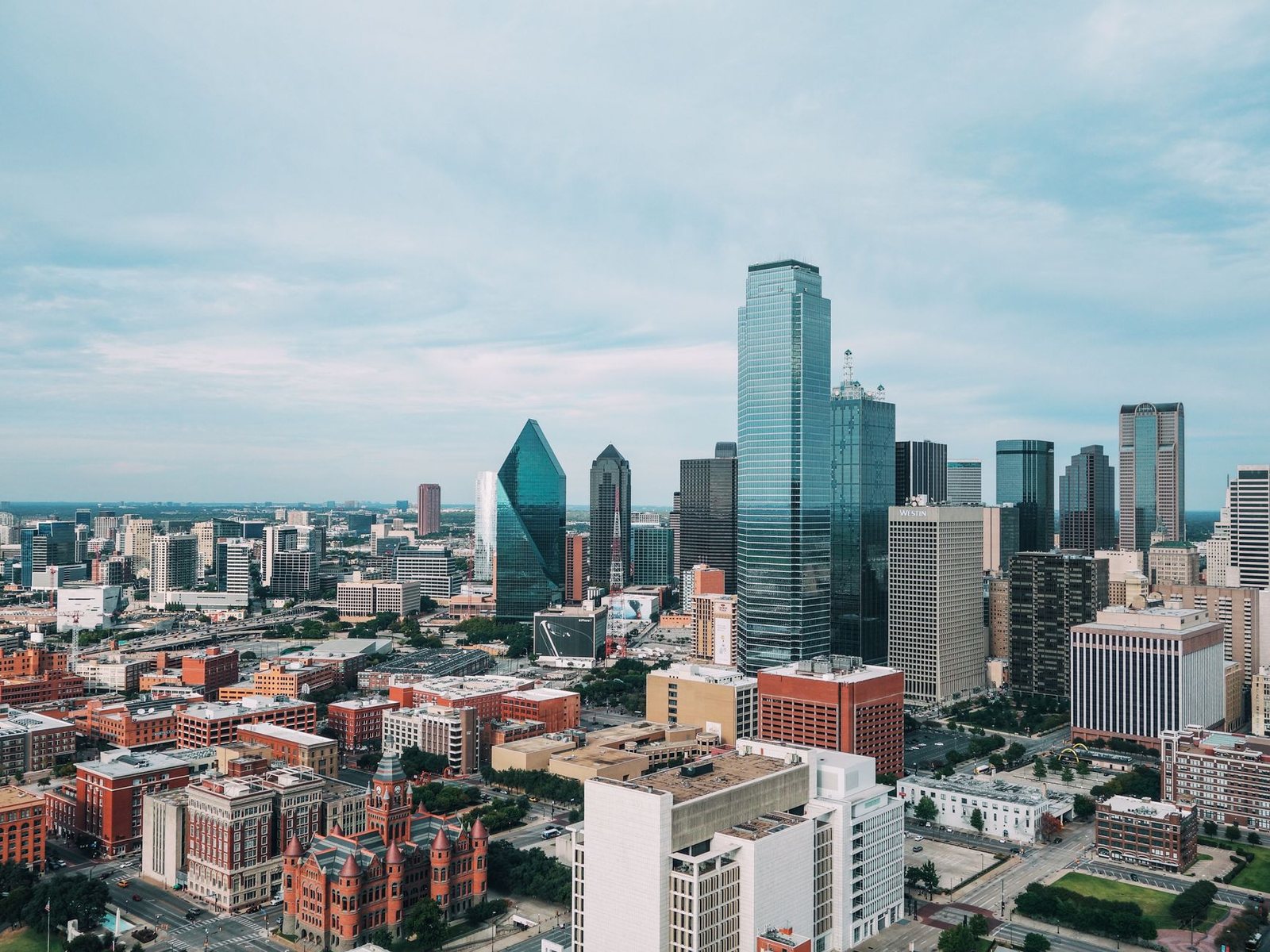 Downtown Dallas skyline seen from above, with the glass towers of the central business district and the red sandstone Old Red Courthouse in the foreground