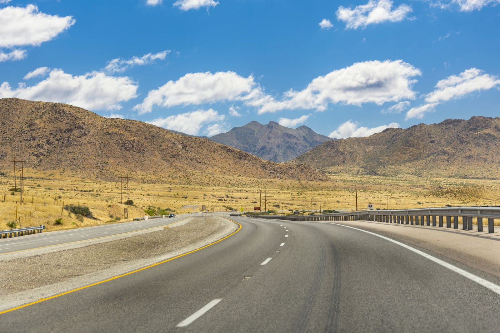 An interstate highway curving through dry desert grassland toward rugged mountains near El Paso under a bright summer sky