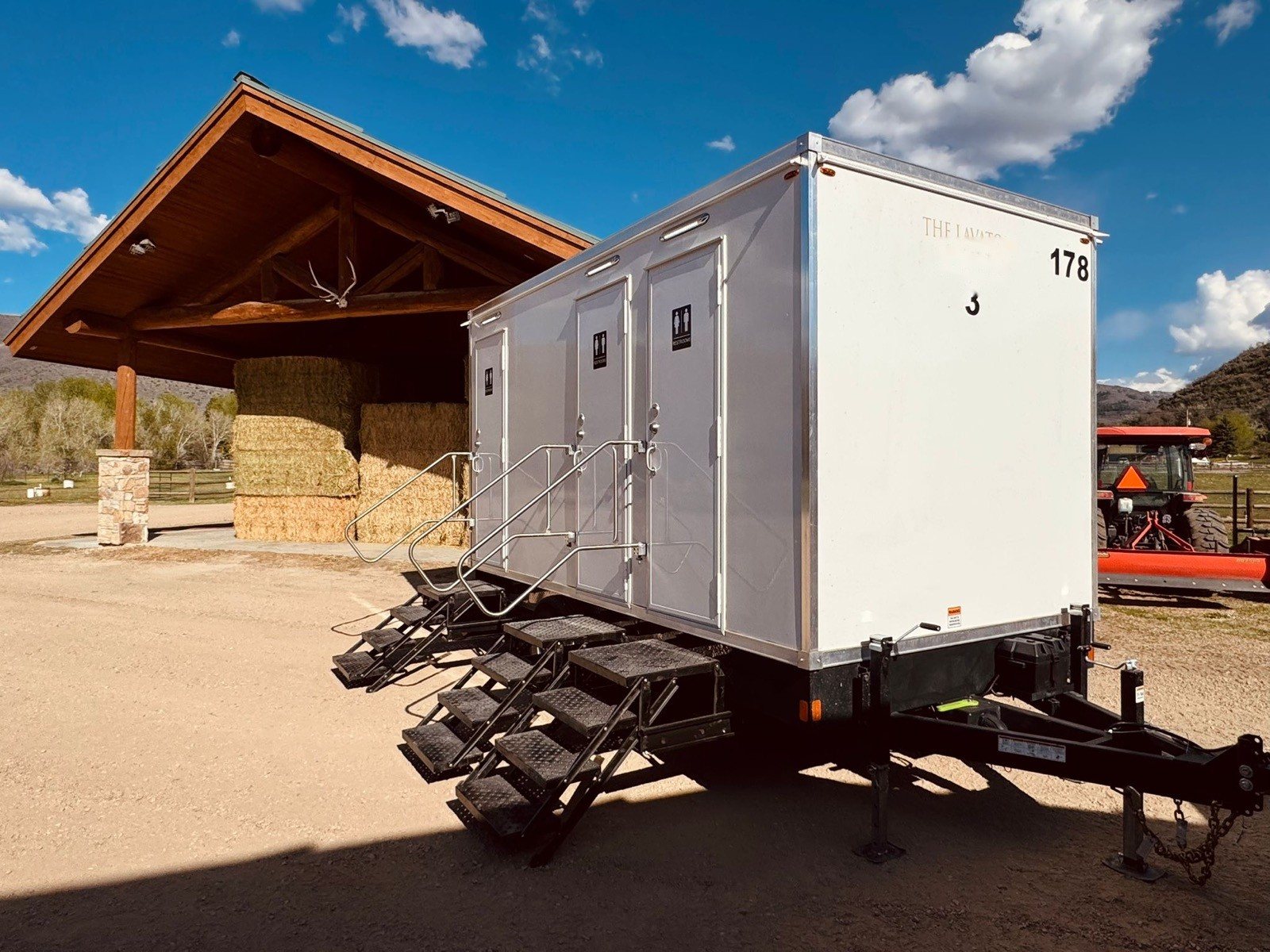 A Lavatory 3-Station restroom trailer next to a timber pavilion at a ranch venue