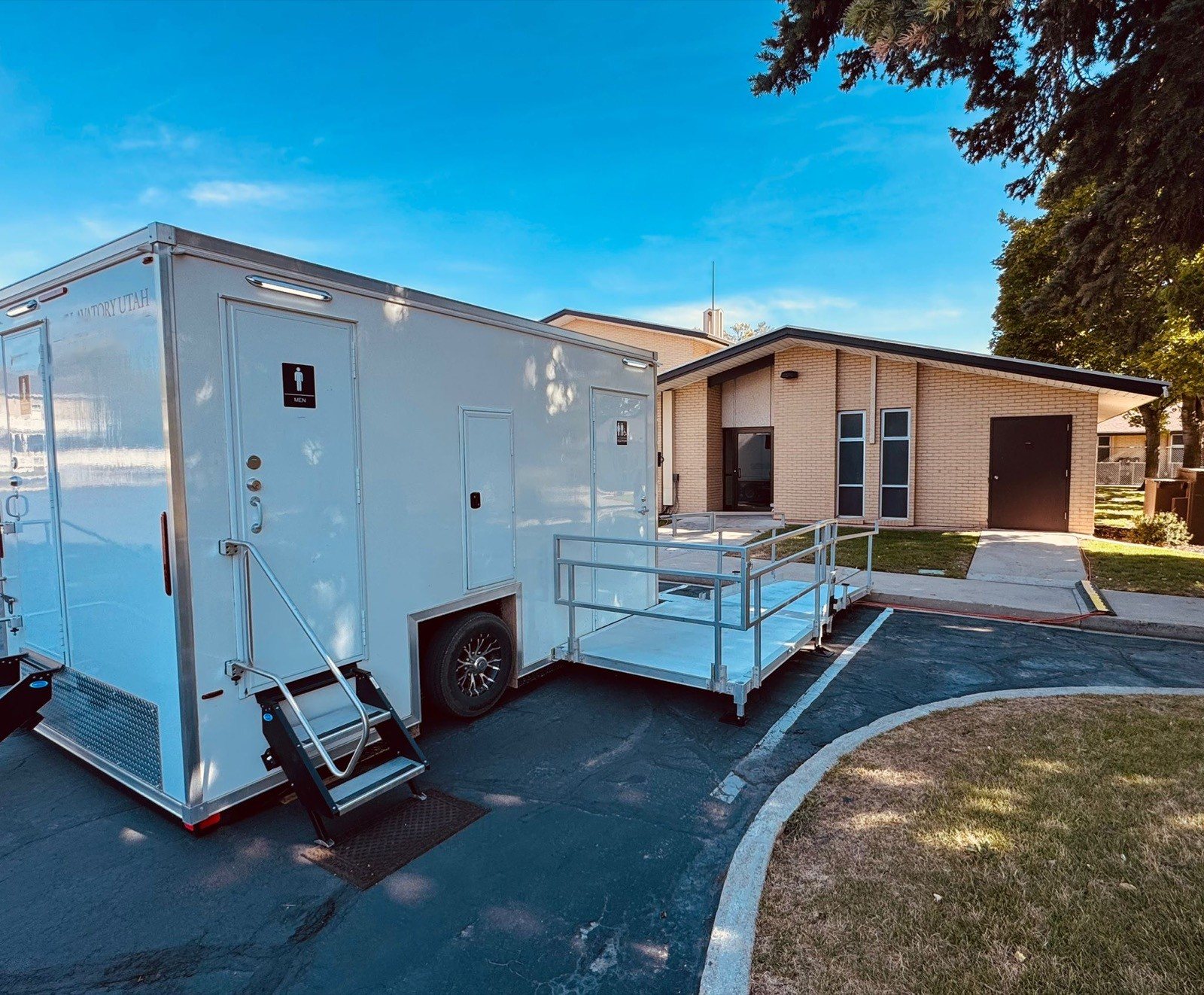 A Lavatory ADA restroom trailer with a long ramp set beside a church building