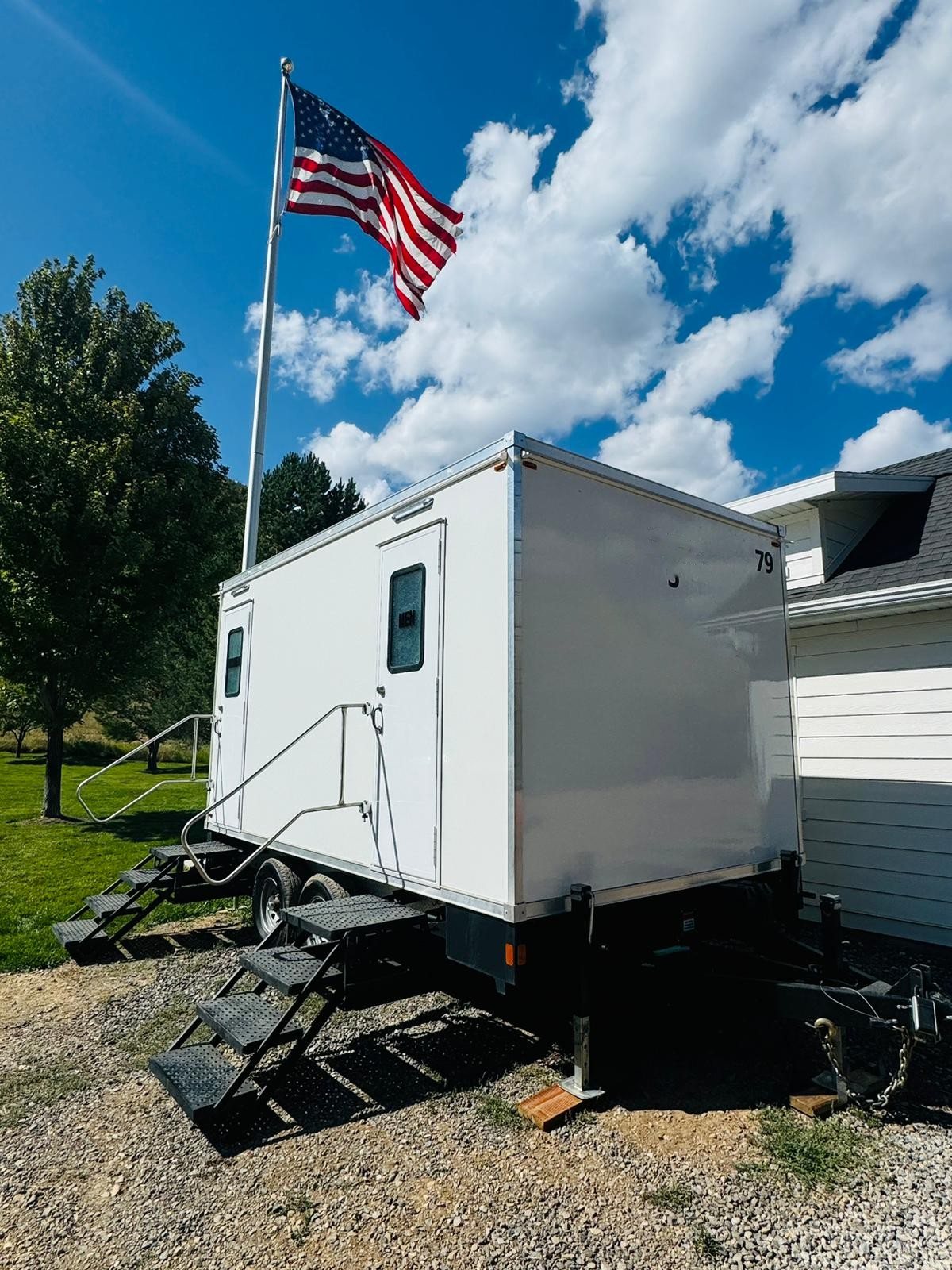 A Lavatory restroom trailer beside a house with an American flag flying overhead