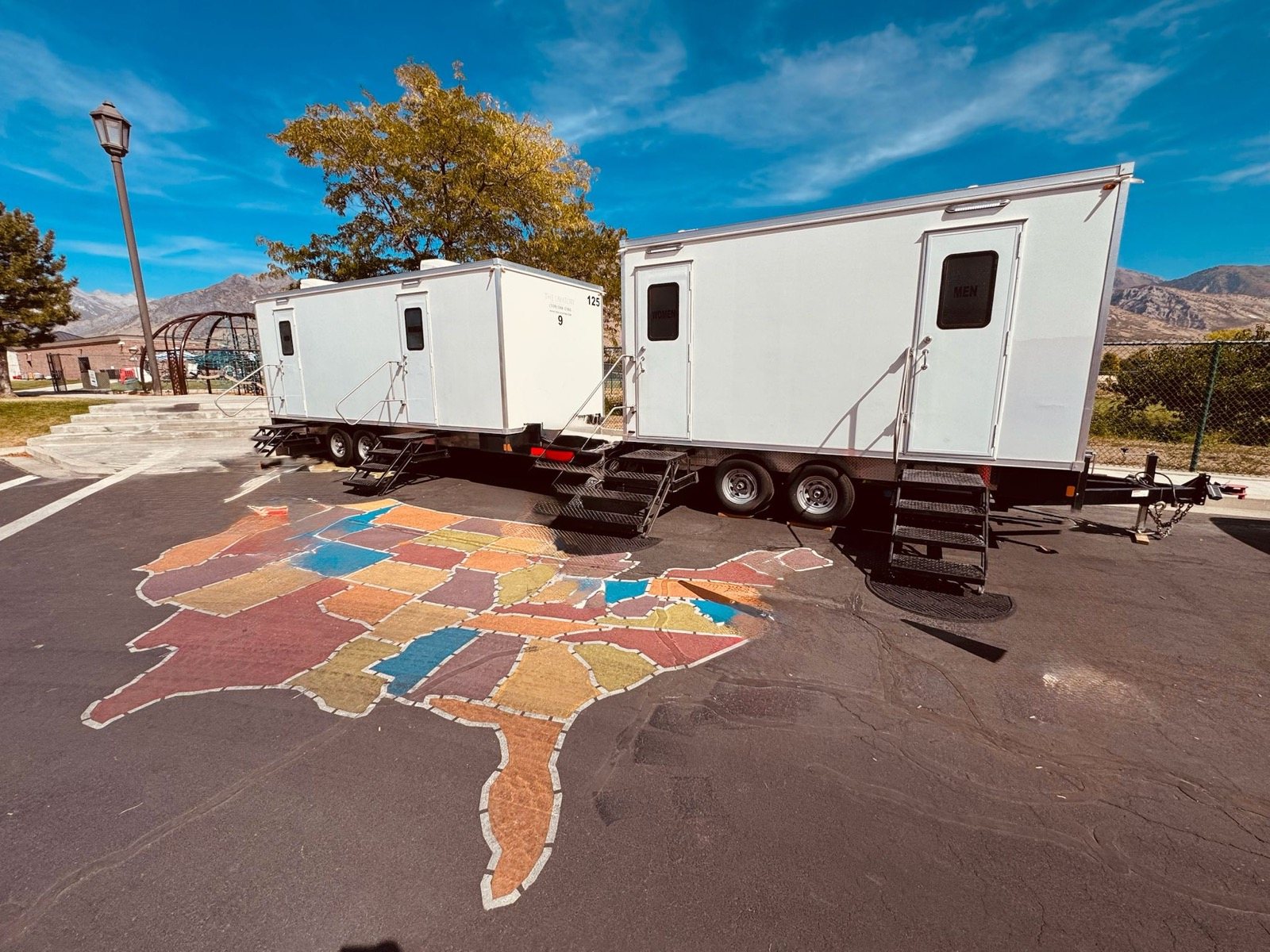 Two Lavatory restroom trailers on a school playground with a painted map of the United States on the blacktop