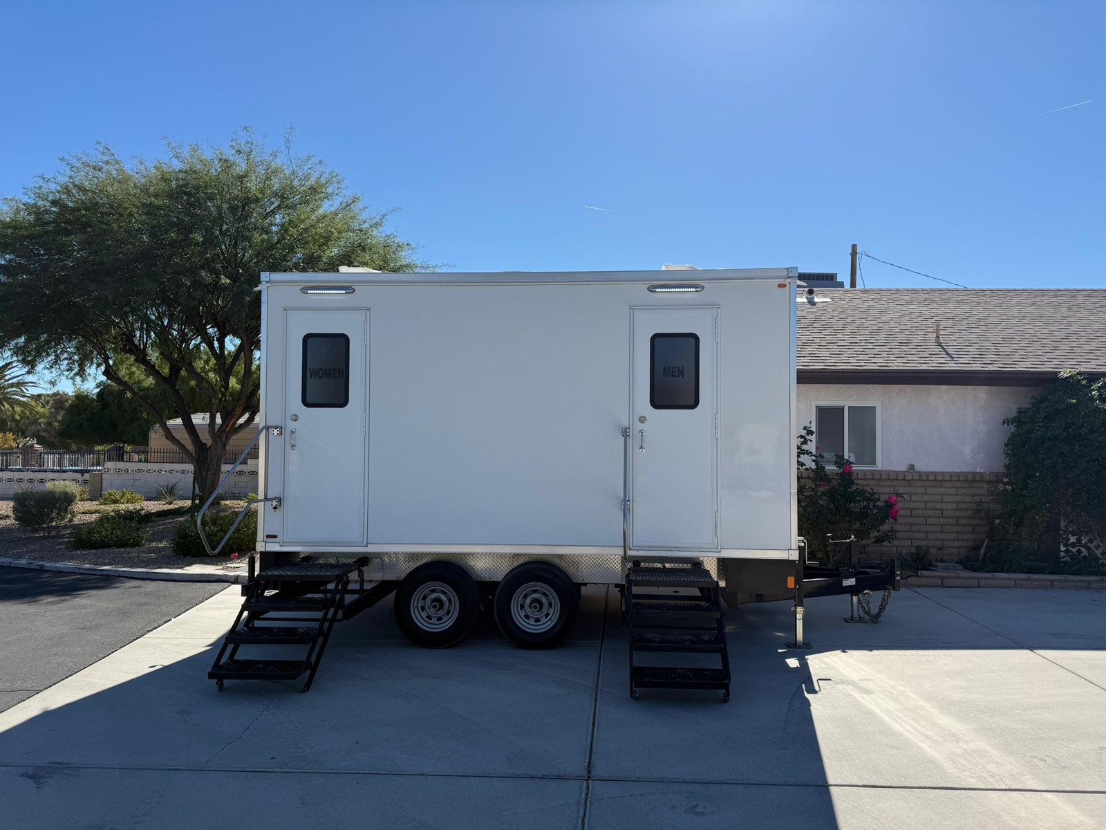 A Lavatory restroom trailer parked in the driveway of a single story desert home with a tile roof