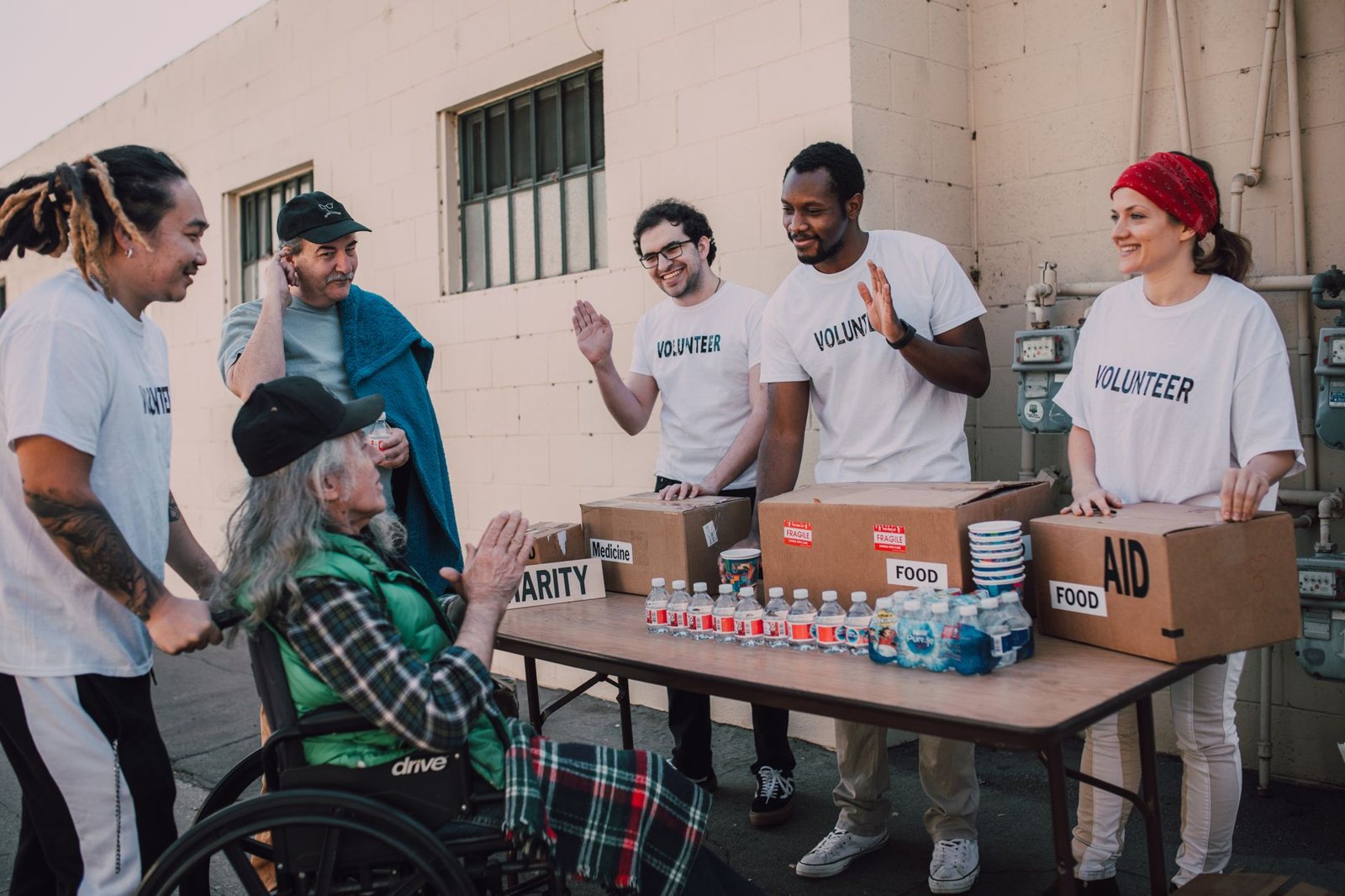 Volunteers in white shirts hand out food, water and supplies from a folding table at an outdoor community aid event