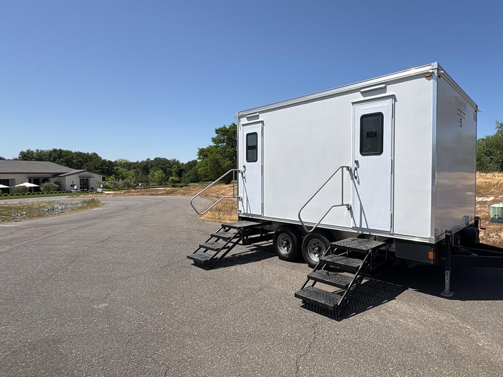 A Lavatory restroom trailer parked on a paved access road beside a graded lot at a new development site