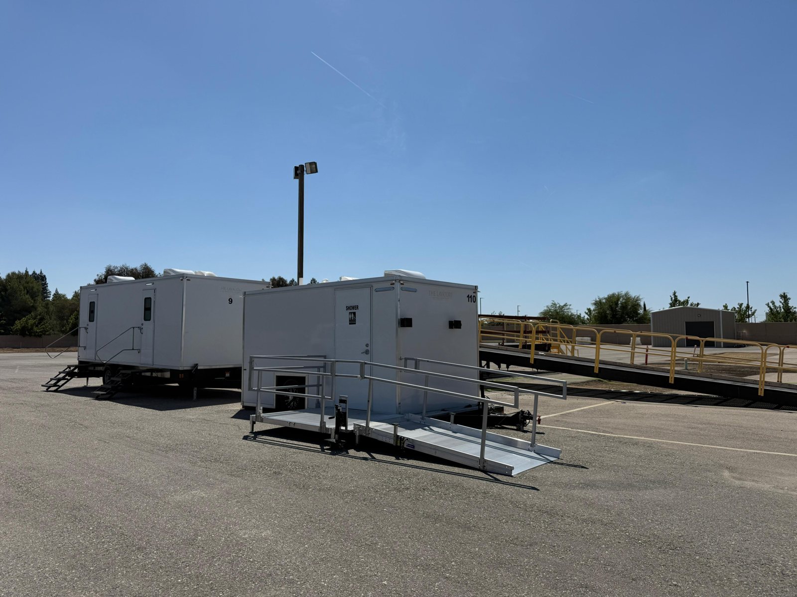 Single-station ADA shower and restroom combo with a long aluminum ramp next to a 2-station trailer on a paved lot in Clovis