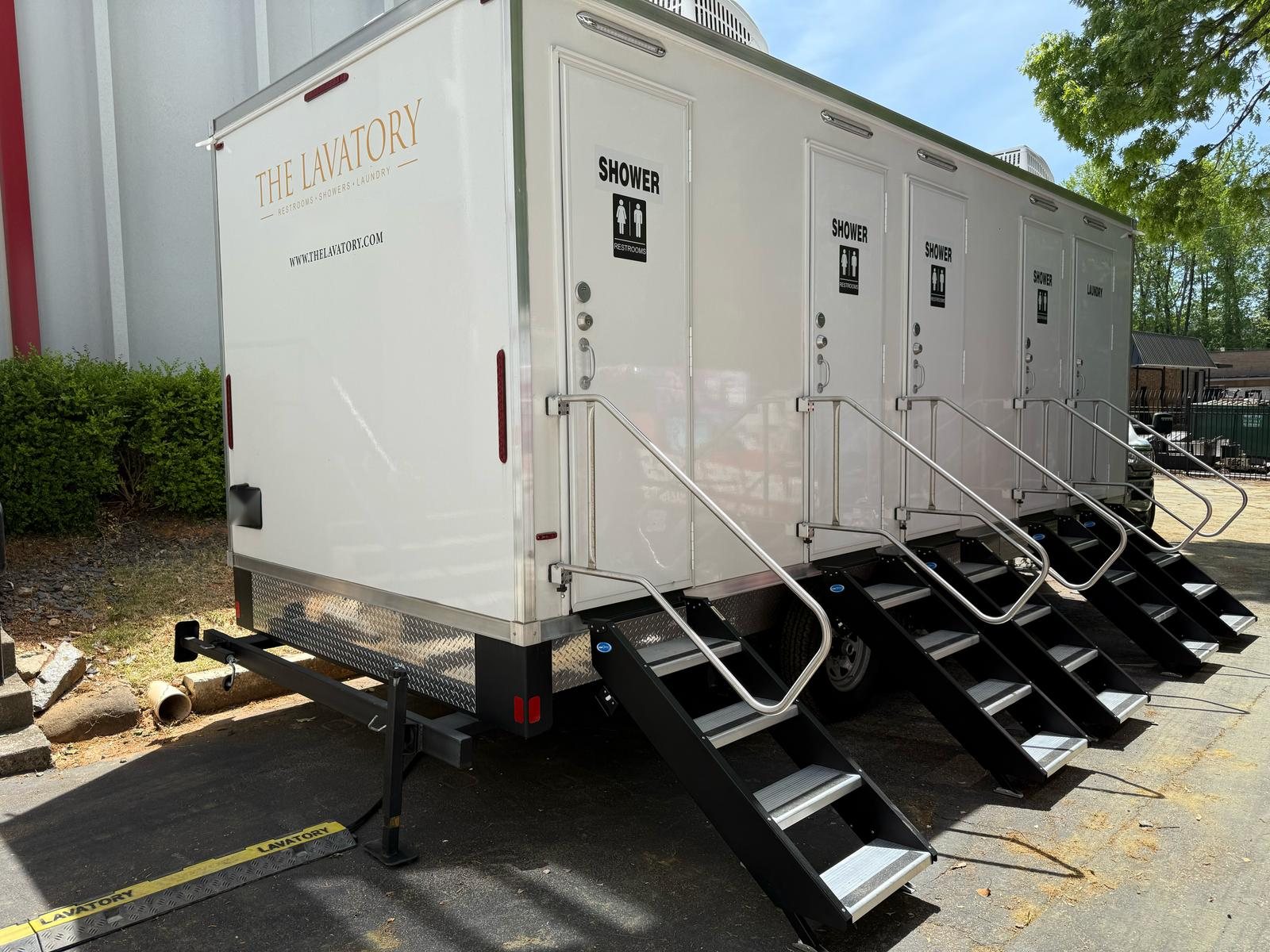 4-station shower, restroom and laundry combo with five doors and stair units on a paved yard beside a large industrial building