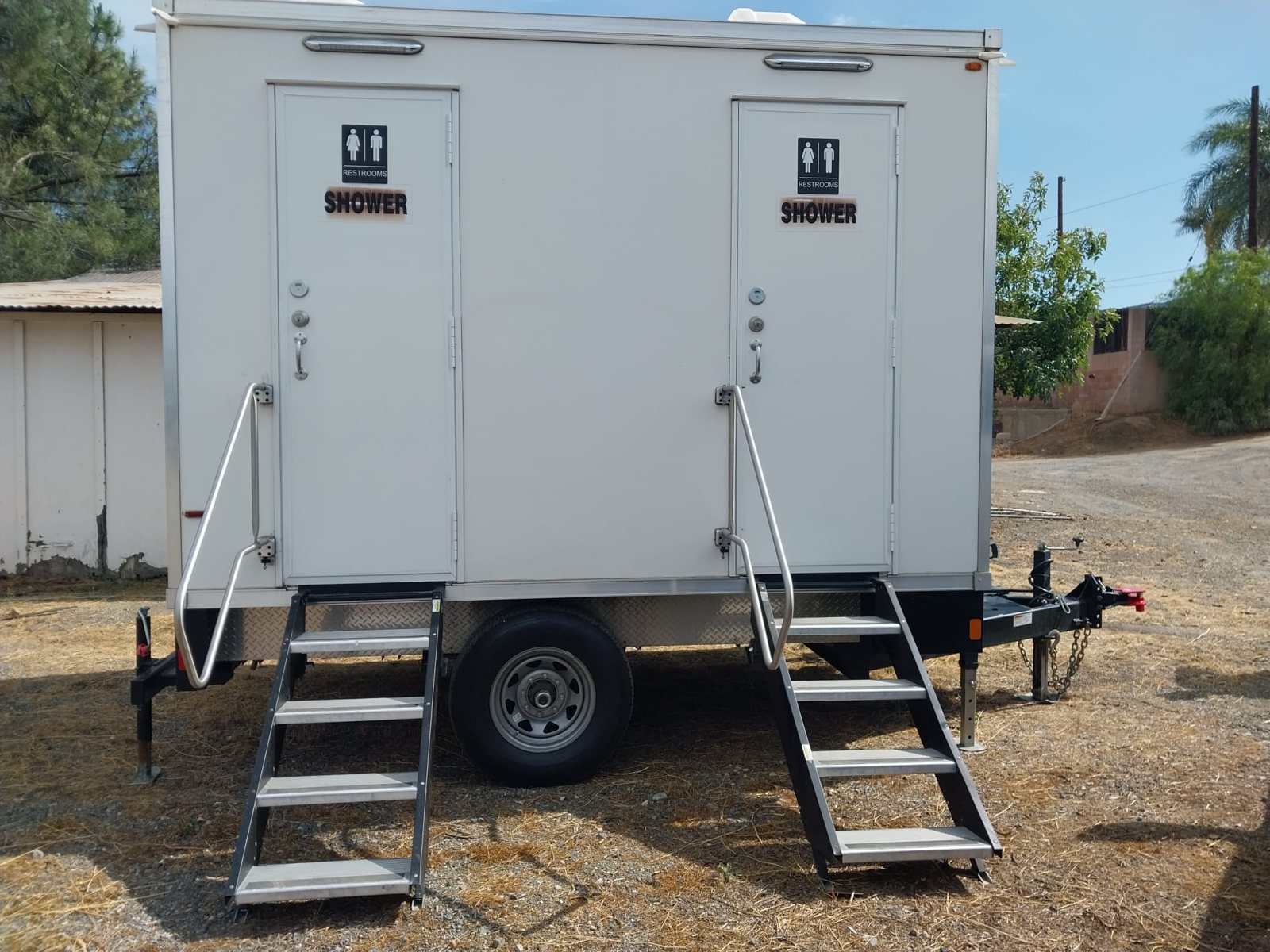 Two-station shower and restroom combo trailer on a dry dirt lot with stairs set at both doors