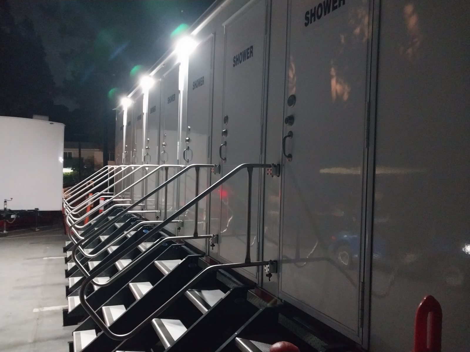 8-station private shower trailer lit up at night on a paved lot, with a railed stair at each SHOWER door