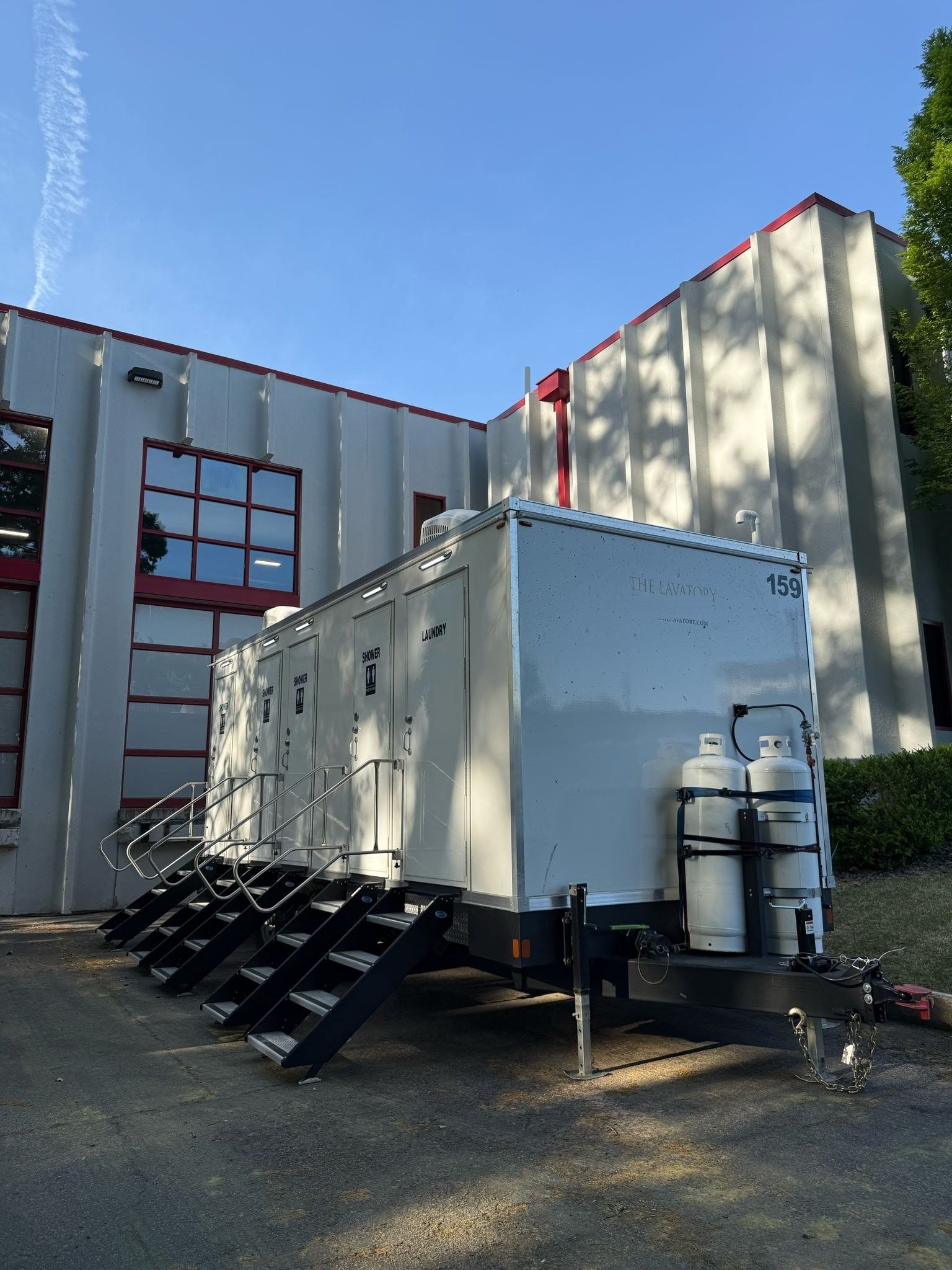 4-station shower and laundry combo trailer parked beside a two-story building, propane tanks on the tongue