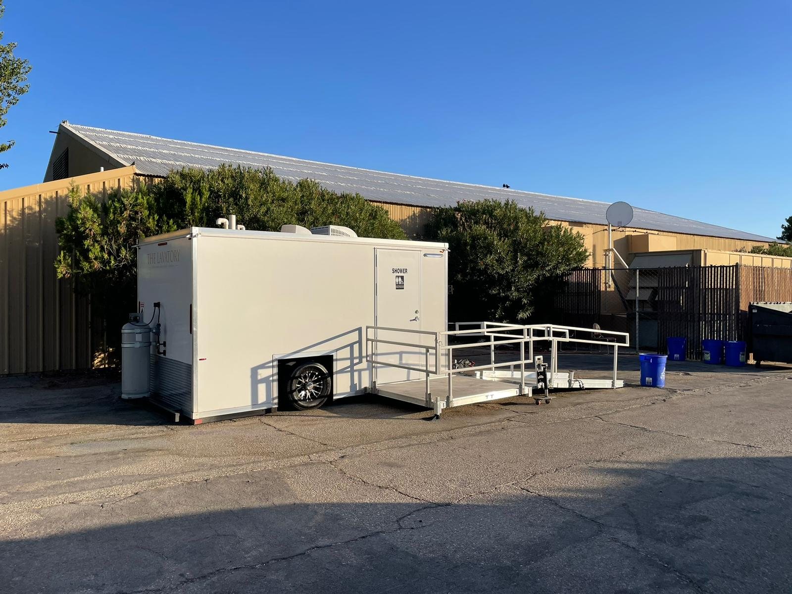 ADA plus two shower trailer with its ramp deployed on the paved yard of a metal industrial building