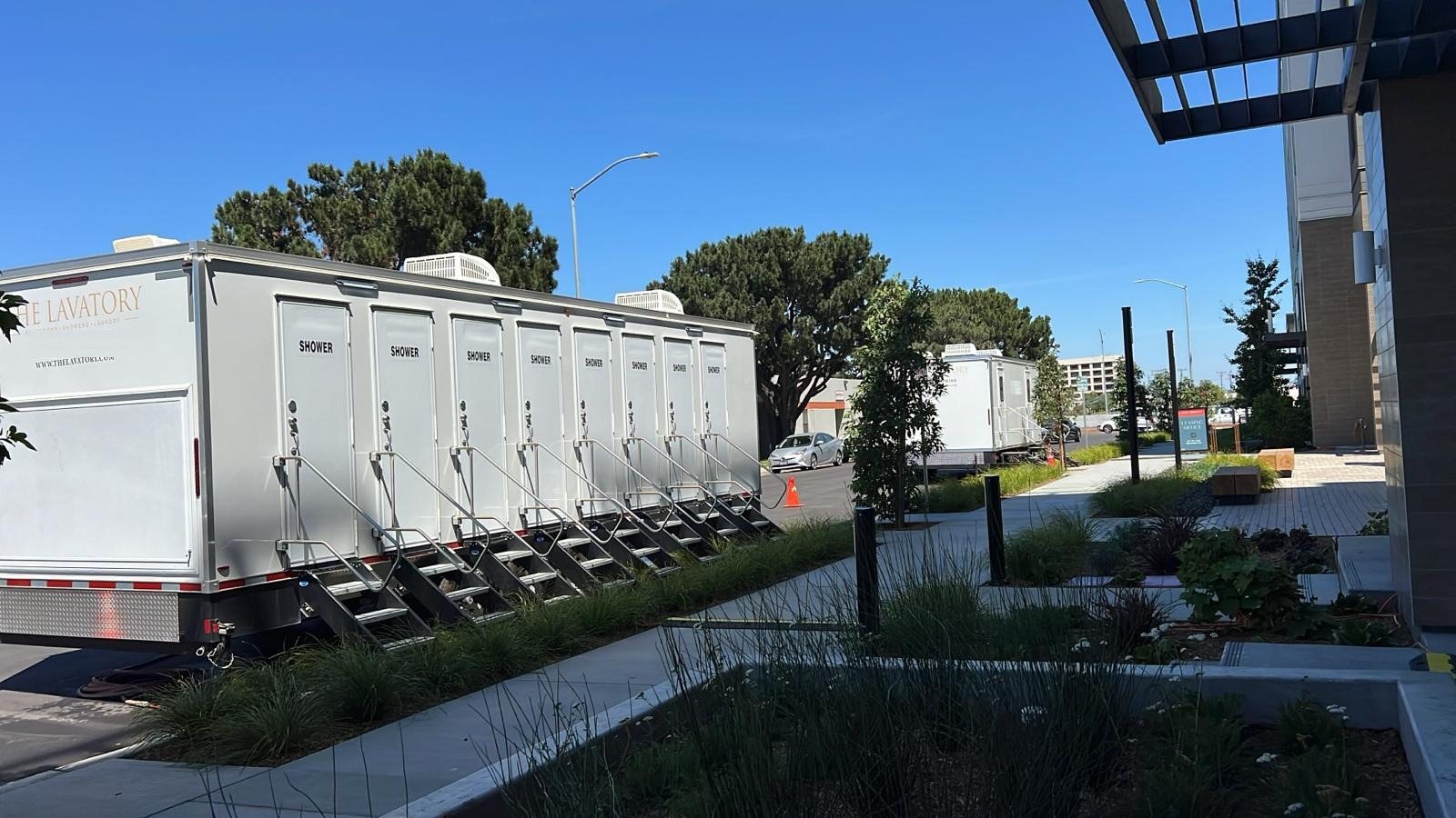 8-station private shower trailer with eight doors and eight stair units parked along a landscaped sidewalk beside a modern office building
