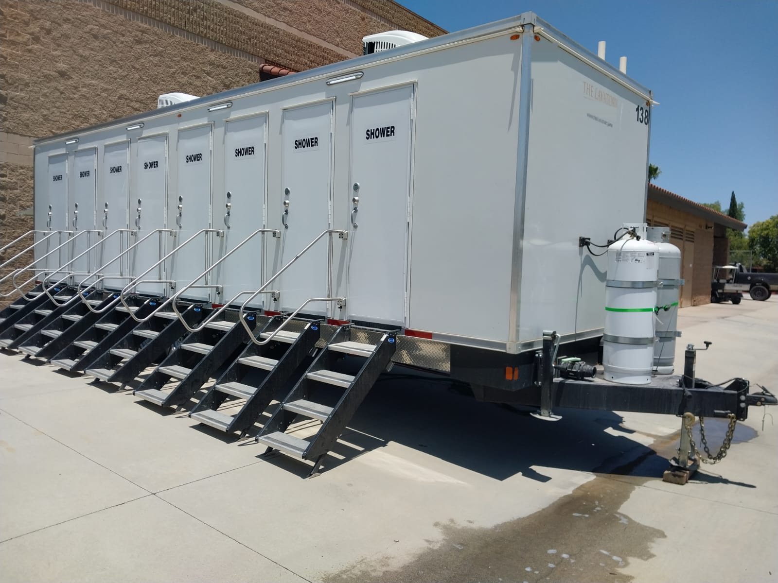 8-station shower trailer with eight private shower doors and eight stair units parked on concrete beside a tan block building