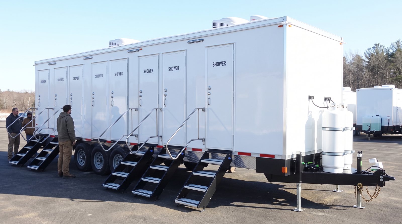 8-station shower trailer on a paved lot with three crew members standing near the stairs and other trailers parked behind