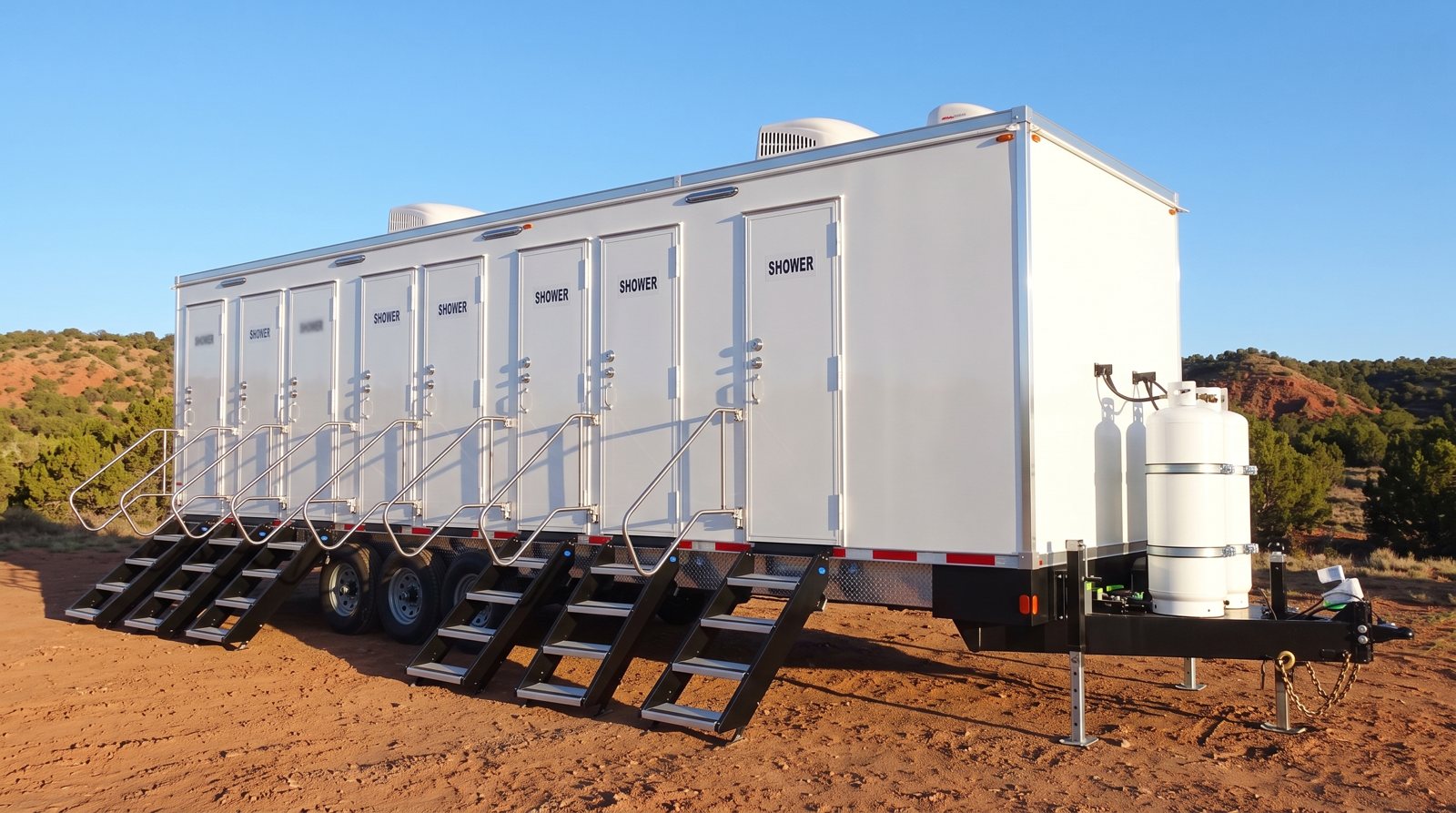 Private 8-station shower trailer on red dirt with pinon and juniper hills behind it, the kind of ground found around Santa Fe, NM