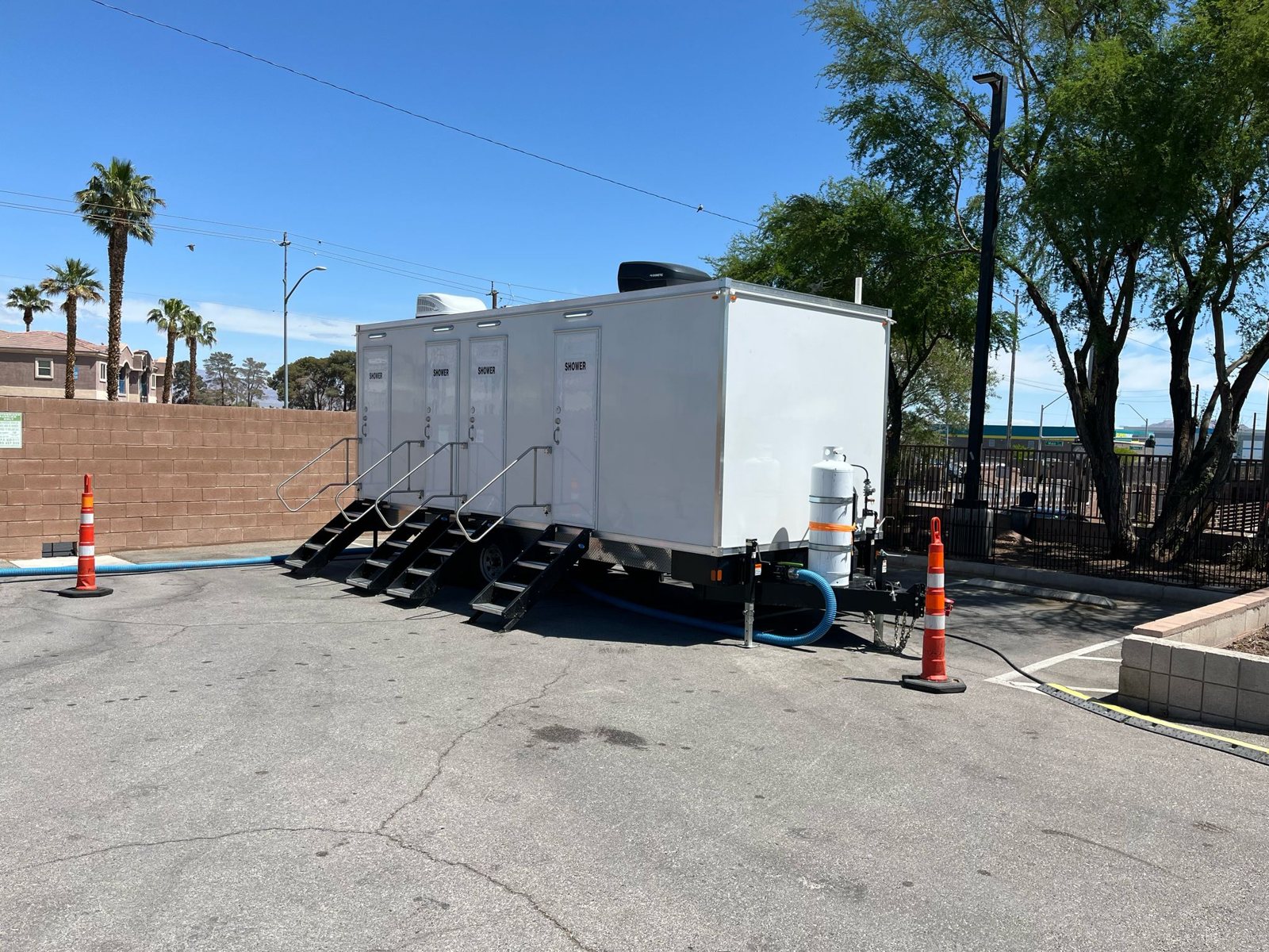 8-station private shower trailer with four stairs and a propane tank, set on a paved lot under overhead power lines with orange cones at each end